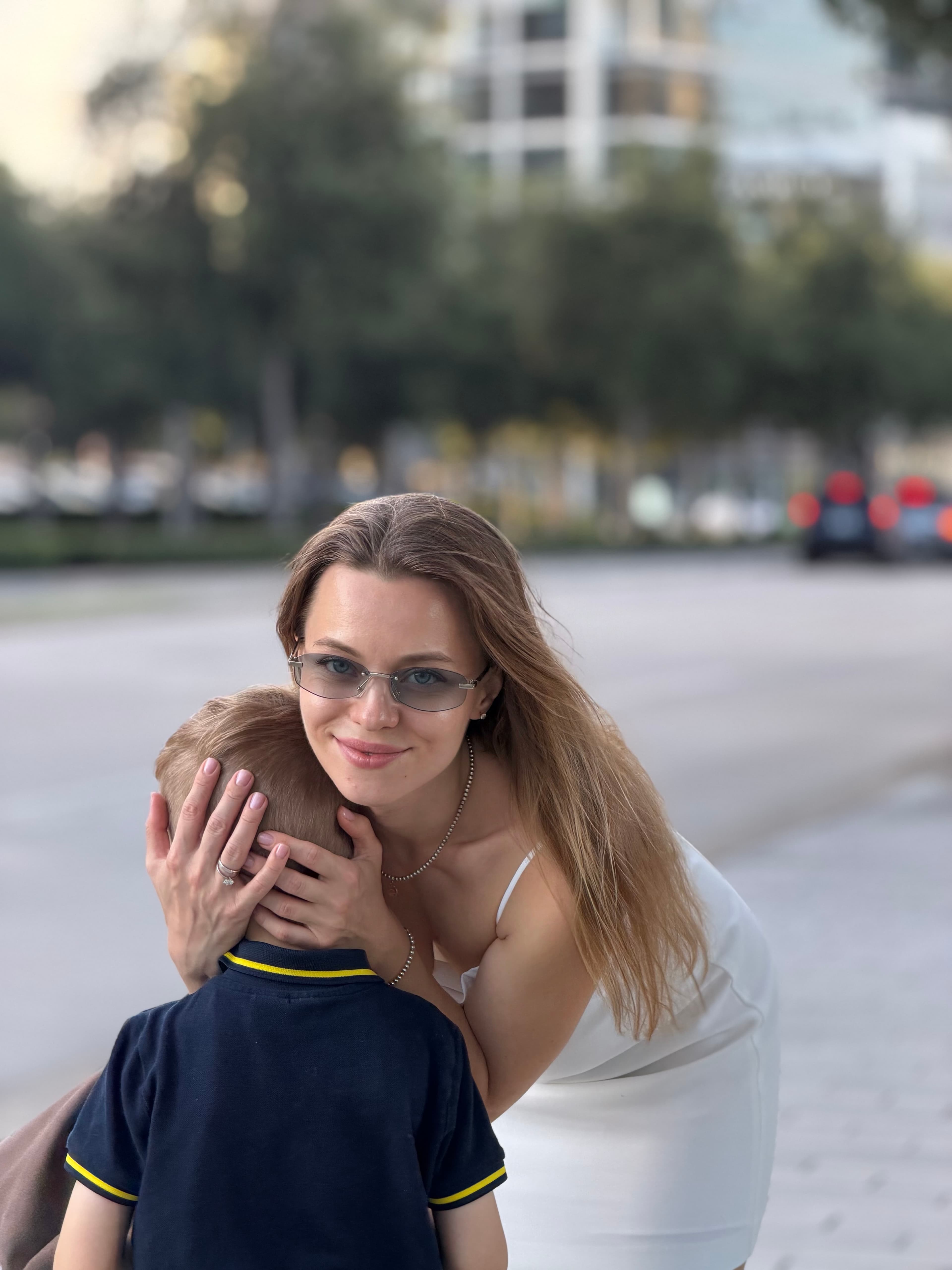 Tania crouching down to hug her son on a city sidewalk.